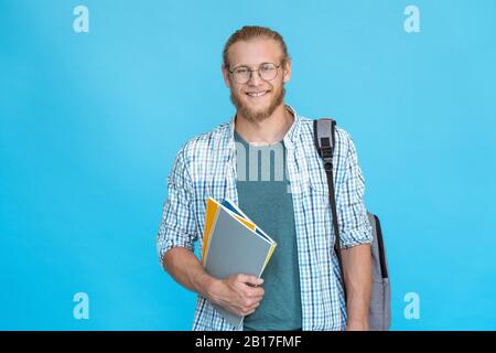 Ritratto studente universitario sorridente in occhiali in piedi tenere copybooks zaino