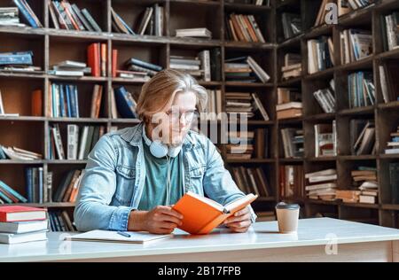 Occhiali da giovane ribassati seri siedono biblioteca leggere libro hobby concetto di istruzione Foto Stock