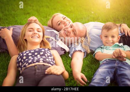 Felice concetto di famiglia. Madre, padre, sole e figlia all'aperto sdraiati su erba prestito sole si flare a destra in una giornata di sole. Foto Stock