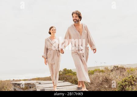 Buona coppia con accappatoi a piedi sul lungomare della costa Foto Stock