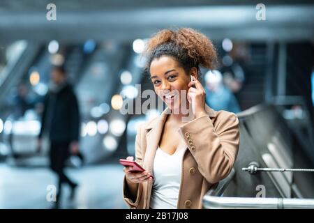 Ritratto di giovane donna felice con telefono cellulare e auricolari alla stazione della metropolitana Foto Stock