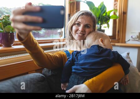 Donna che prende un selfie con il suo figlio sonno carino sul divano Foto Stock