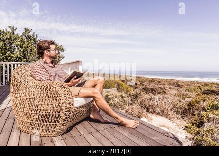 Uomo che legge un libro su un ponte sulla costa Foto Stock