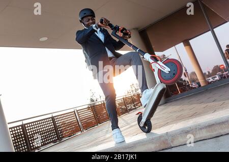 Uomo d'affari sorridente con scooter al tramonto Foto Stock