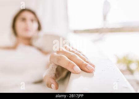 Mano di giovane donna che si rilassa nella vasca da bagno Foto Stock