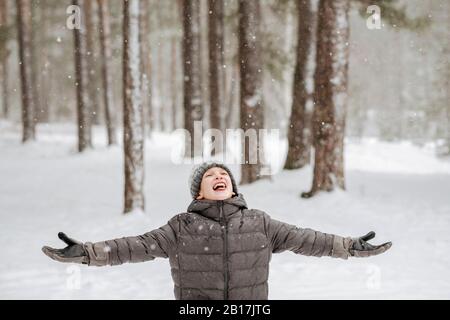 Ritratto di ragazzo che cattura fiocchi di neve nella foresta invernale Foto Stock