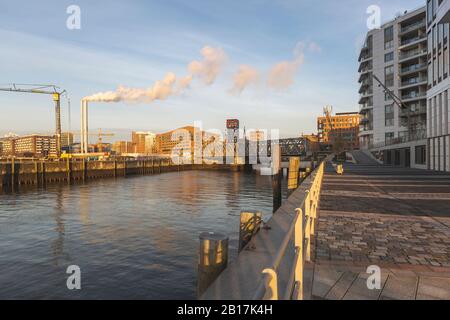 Germania, Amburgo, HafenCity porto all'alba con fumo che esce dai camini industriali in background Foto Stock