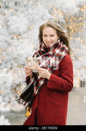 Ritratto di giovane donna sorridente in piedi sulla strada con carta di Natale di fronte agli alberi bianchi di Natale Foto Stock