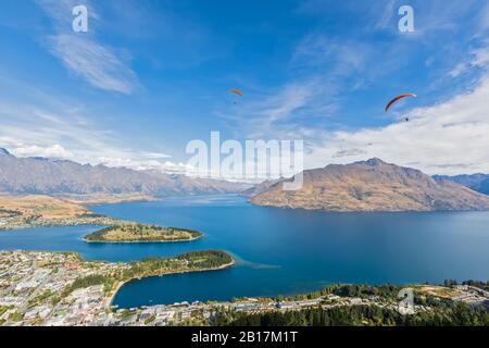Nuova Zelanda, Otago, Queenstown, Paraglatori che volano sulla città di Lakeshore con montagne sullo sfondo Foto Stock