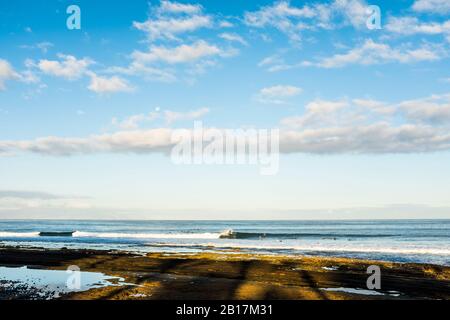 Spiaggia vista oceano con molti surfisti in acqua in attesa onde per godere l'attività sportiva natura - persone attive al mare - isola in background - Foto Stock
