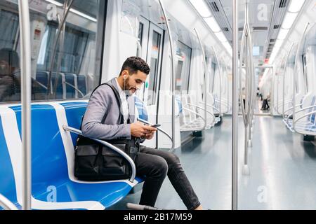 Giovane uomo d'affari con cellulare e cuffie sulla metropolitana Foto Stock