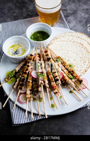 Spiedini di carne su piatto con yogurt e salsa di prezzemolo con pane piatto e verdure Foto Stock