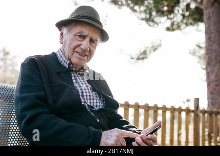 Vecchio con, seduto su banco, utilizzando lo smartphone Foto Stock