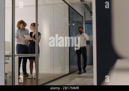 Uomo d'affari e donna d'affari che usano il tablet in ufficio con l'uomo d'affari sul telefono che passa Foto Stock