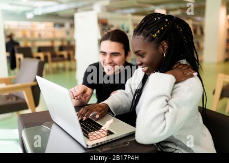 Due studenti sorridenti che usano il laptop in una biblioteca Foto Stock