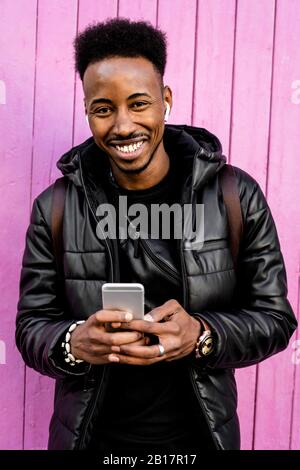 Ritratto di uomo sorridente con smartphone e auricolari wireless all'aperto Foto Stock