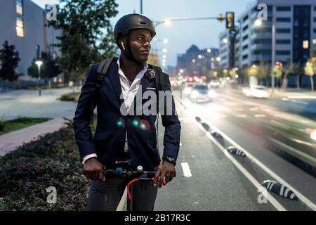 Ritratto di uomo d'affari con scooter a spinta sulla pista ciclabile in serata Foto Stock