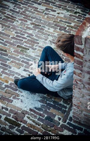 Adolescente che usa lo smartphone, seduto su un pavimento in pietra Foto Stock