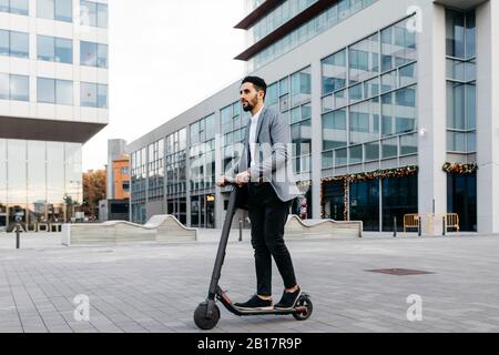 Casual giovane uomo d'affari a cavallo scooter elettrico in città Foto Stock