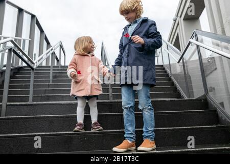 Fratello e sorella con lecca-lecca che si alzano sulle scale in un giorno di pioggia Foto Stock