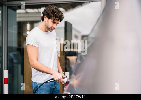 Uomo che carica un'auto elettrica in una stazione Foto Stock