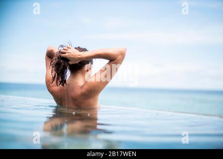Vista posteriore della donna in piscina a sfioro, Isola di Maguhdhuvaa, Atollo di Gaafu Dhalu, Maldive Foto Stock