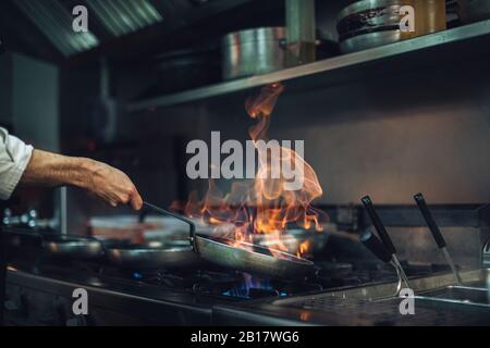 Lo chef prepara un piatto flambato alla stufa a gas nella cucina del ristorante Foto Stock