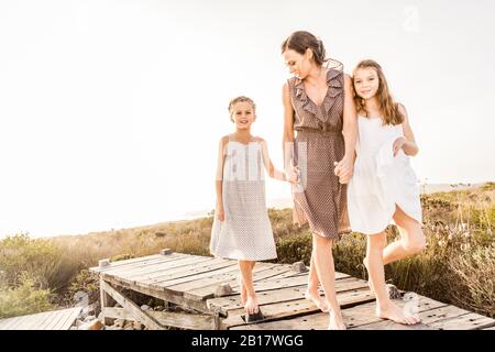 Madre che cammina con le sue due figlie su una passerella al tramonto Foto Stock