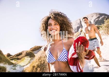 Portait di giovane donna sorridente sulla strada per la spiaggia con l'uomo in background Foto Stock