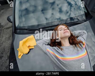 Donna rossa sdraiata sul cofano dell'auto Foto Stock