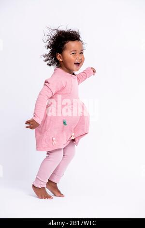 Ritratto di bambina a piedi nudi vestita con un salto rosa davanti a sfondo bianco Foto Stock