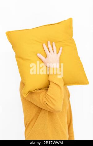 Uomo che indossa il pullover giallo che nasconde il viso dietro il cuscino giallo Foto Stock