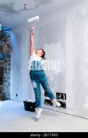 Ragazza che salta mentre dipingi un muro in una casa Foto Stock