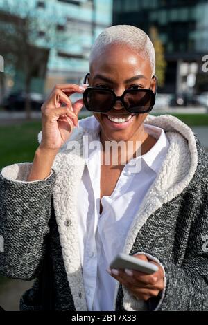 Elegante busnesswoman che si trova in città, con smartphone Foto Stock