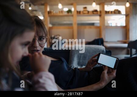 Donna e ragazza seduti sul divano in ufficio utilizzando lo smartphone Foto Stock