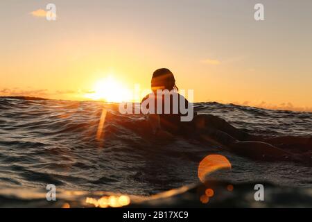 Surfista che si stende sul surf al tramonto, Bali, Indonesia Foto Stock