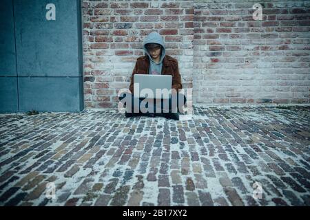 Adolescente che usa il laptop e seduto su un pavimento in pietra in città Foto Stock