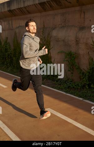 Uomo che corre su una strada alla luce del sole Foto Stock