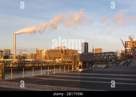 Germania, Amburgo, HafenCity porto all'alba con fumo che esce dai camini industriali in background Foto Stock