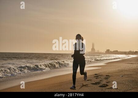 Giovane donna che corre sulla spiaggia al tramonto Foto Stock