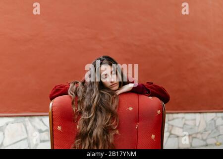 Ritratto di giovane donna con lunghi capelli castani appoggiato sul retro della poltrona rossa Foto Stock