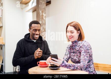Uomo e donna sorridenti con cellulare in un caffè Foto Stock