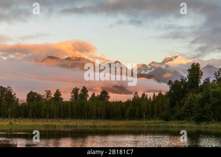 Nuova Zelanda, Westland District, Fox Glacier, Lake Matheson all'alba con montagne avvolte in nebbia sullo sfondo Foto Stock