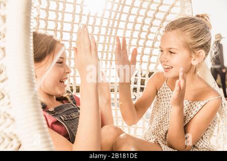 Due ragazze che si aggrappano le mani sulla sedia sospesa Foto Stock