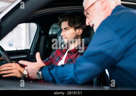 Concessionario auto che mostra l'auto al giovane uomo nello showroom Foto Stock