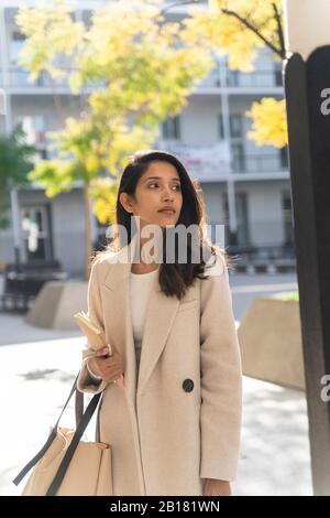 Giovane donna con libro in città guardando intorno Foto Stock