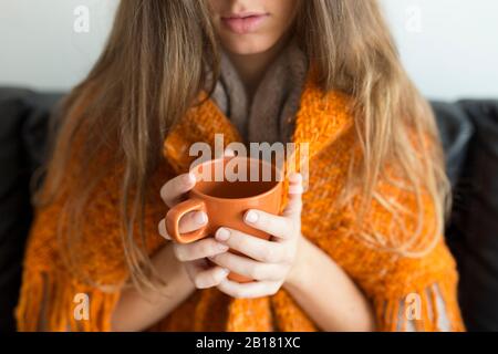 Vista del raccolto della giovane donna seduta sul divano tenendo la tazza arancione Foto Stock