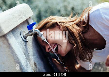 Ragazza adolescente felice bere acqua da un pozzo Foto Stock