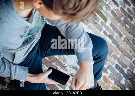 Adolescente che usa lo smartphone, seduto su un pavimento in pietra Foto Stock