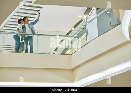 Giovane coppia asiatica che prende selfie nel centro commerciale dopo aver fatto acquisti in vendita Foto Stock